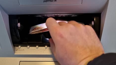 a man's hand places banknotes in an atm receiver. 5000.