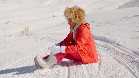 mujer en traje de nieve naranja sentada en la pendiente de esquí