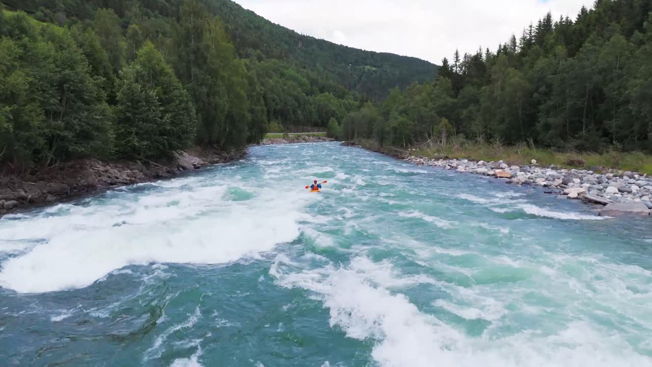 Vista aerea di un canoista che naviga rapide di acque bianche attraverso un fiume pittoresco circondato da vegetazione lussureggiante e montagne