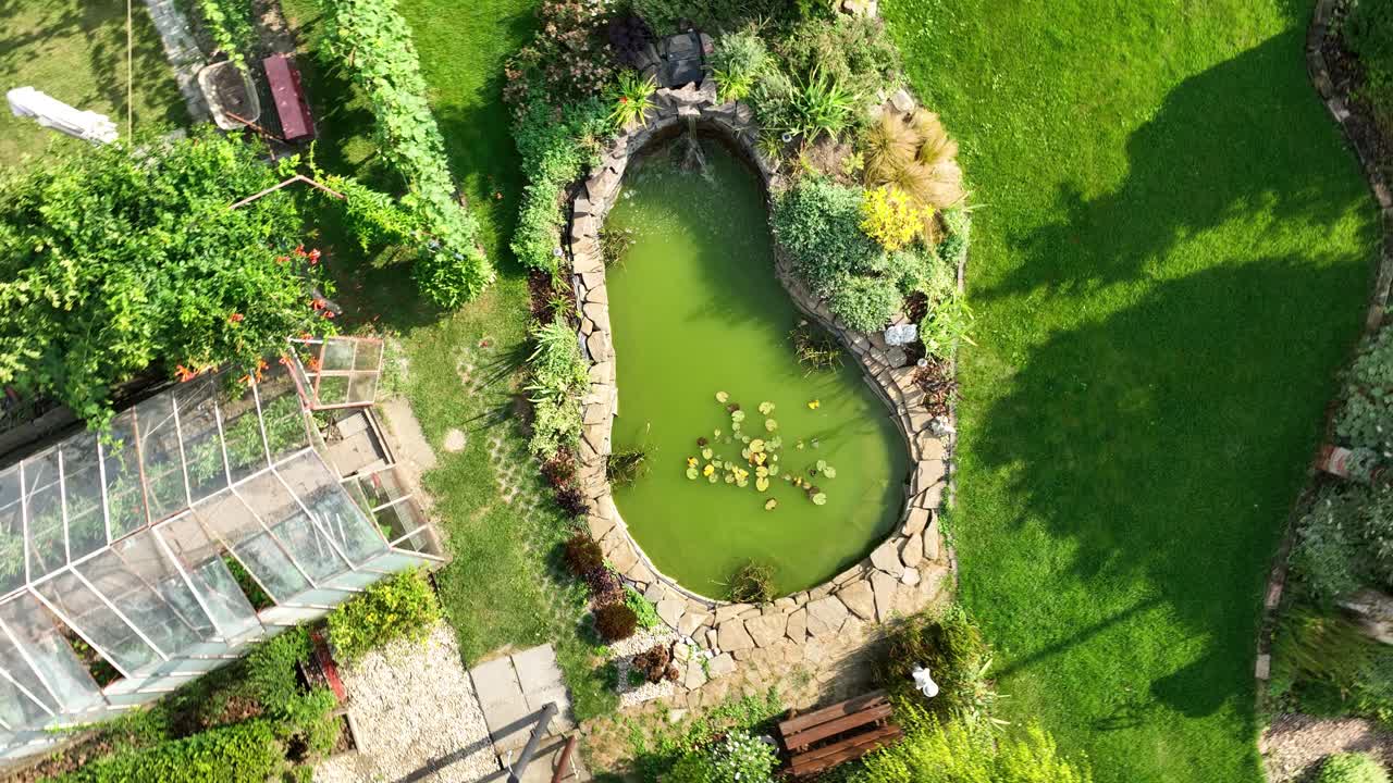 Aerial View of a Green Garden with Pond and Greenhouse