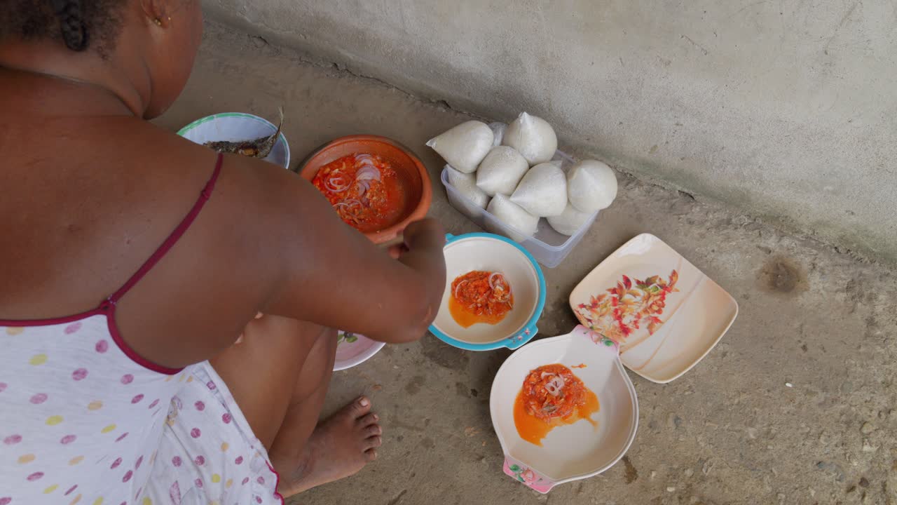 Donna ghanese che cucina, serve stufato e pesce su un piatto accompagnato da banku, tipico gnocco ghanese