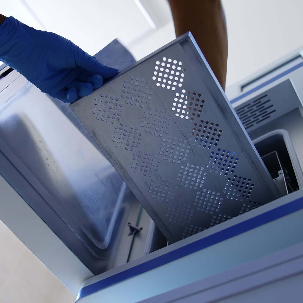 Nurse's gloved hands open the doors of sterilizer. Medic places instrument in plastic bag to a modern disinfection equipment. Low angle view
