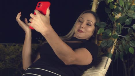 mujer atractiva recostada en un columpio al aire libre por la noche tomando un selfie