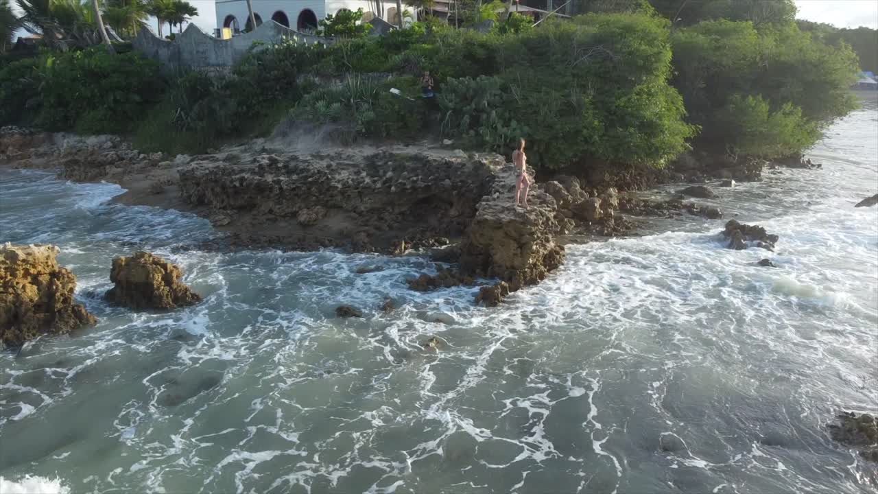 niña de pie sobre una roca en el borde del océano de brasil se asoma al atardecer