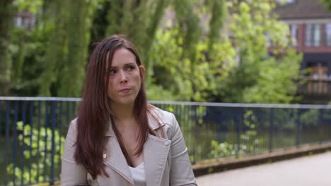 stressed and worried woman outdoors with financial worries about cost of living crisis debt and paying bills in city park