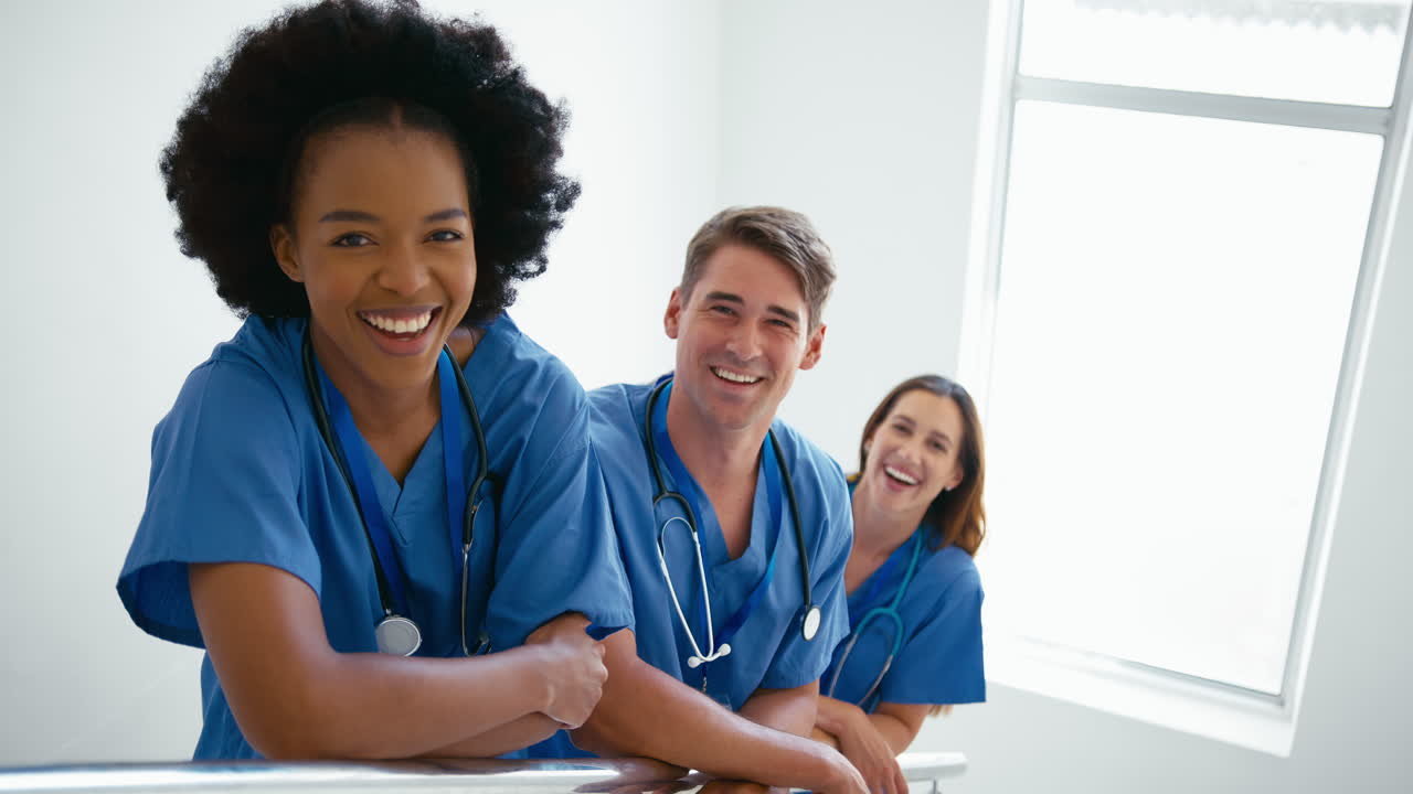 Portrait Of Smiling Multi Cultural Medical Team Wearing Scrubs Standing On Stairs In Hospital