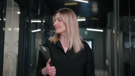 Portrait-of-a-smiling-Business-woman-a-blonde-30-40-years-old-in-a-black-shirt-walking-down-the-corridor-of-a-business-center