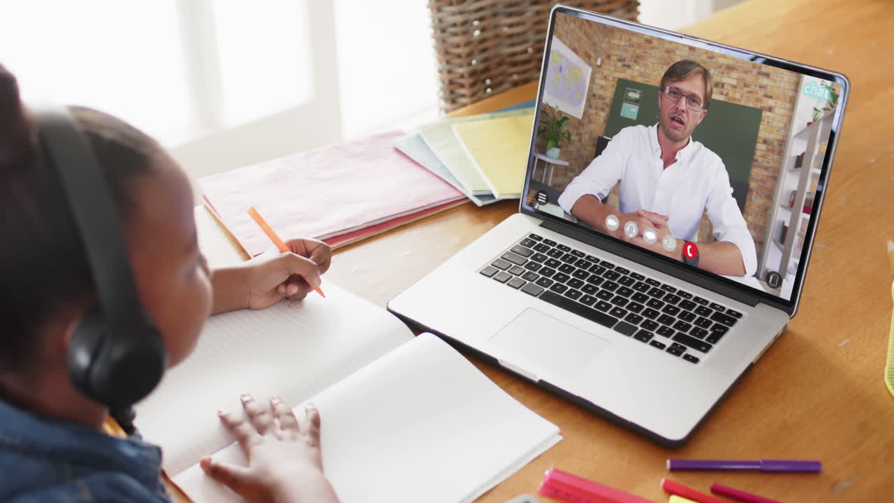 chica afroamericana usando una computadora portátil para una lección en línea con un profesor caucásico en la pantalla