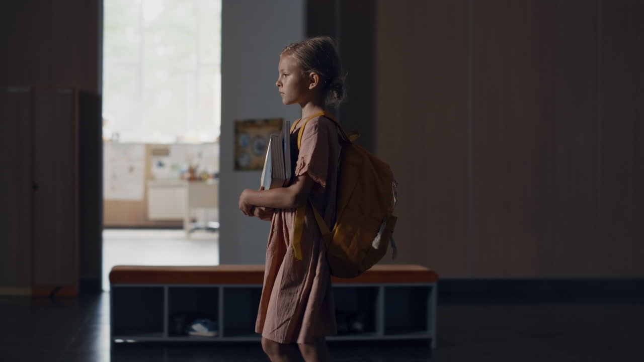 Tensed schoolgirl walking hall full students. Girl holding books going on break.