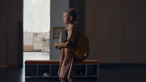 tensed schoolgirl walking hall full students. girl holding books going on break.