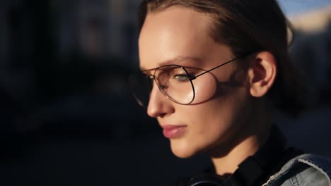 Blonde-Frau-Mit-Transparenter,-Moderner-Brille,-Die-An-Einem-Sonnigen-Tag-Auf-Der-Straße-Spaziert.-Schaut-In-Die-Kamera.-Nachdenklicher-Blick