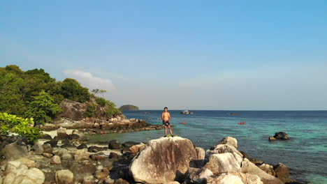 Imágenes-Aéreas-De-Una-Pequeña-Isla-Volando-Lejos-De-Un-Hombre-Blanco-Sin-Camisa-En-La-Cima-De-Las-Rocas