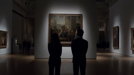 two people observe a large painting in a dimly lit art gallery