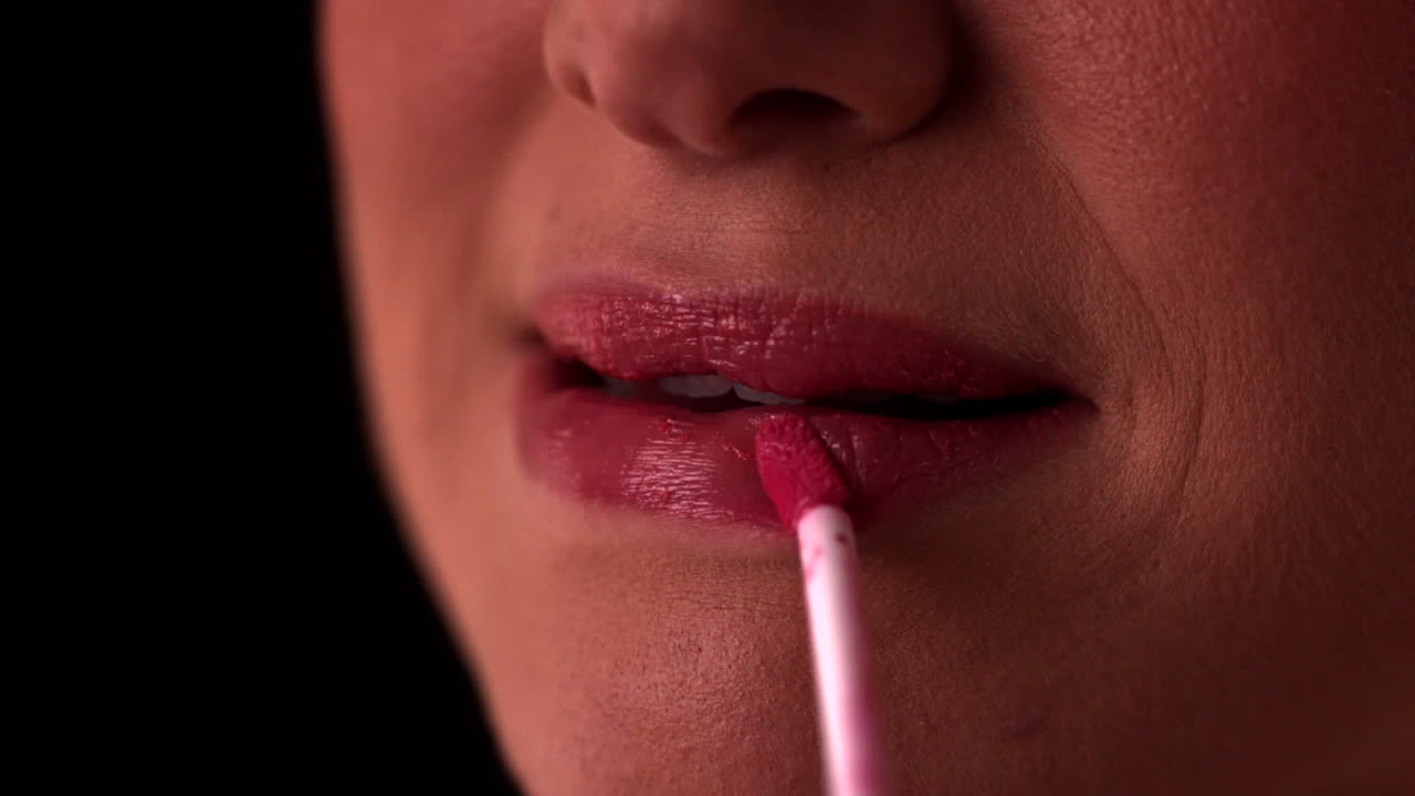mujer aplicando brillo rosa para los labios