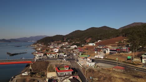 Cars passing bridge and streets on coastal town of Namhae, housing area, forested hills. South Korea cityscape - aerial