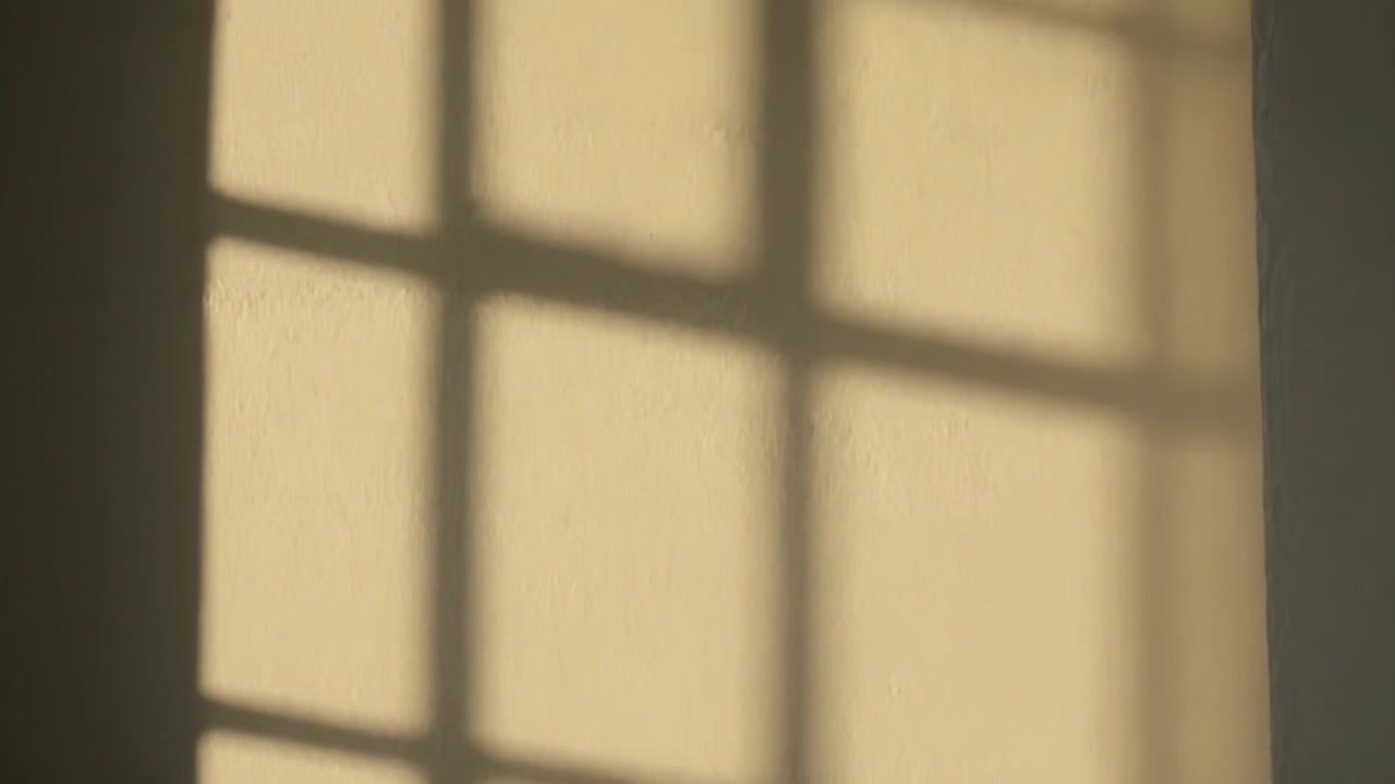 Shifting multi-pane window shadow sliding across textured wall at home, sunlight angle shifting