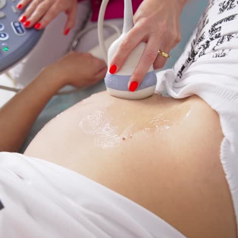 Making ultrasound of baby in clinic office. Pregnant woman laying on bed during ultrasound. Doctor gynecologist performing screening belly of pregnant woman. Top view