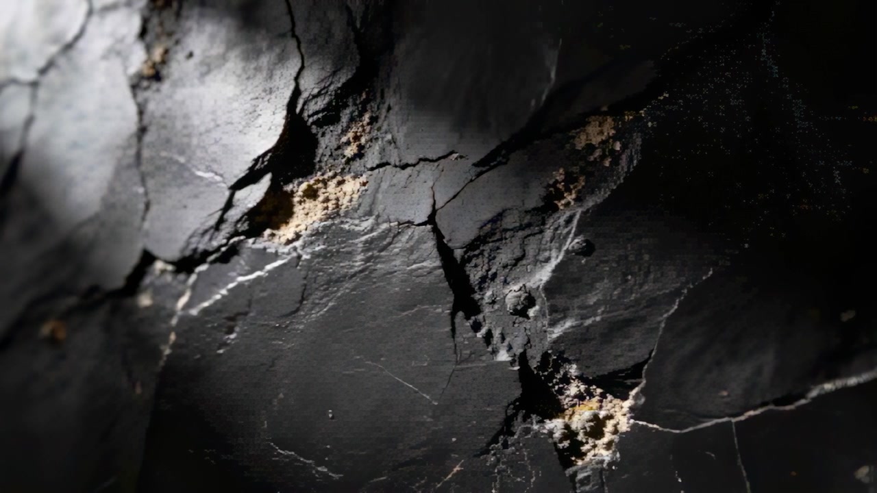 Licht fällt von oben links, eine zerklüftete dunkle Felsplatte legt körnige Ablagerungen an der Höhlenwand frei.