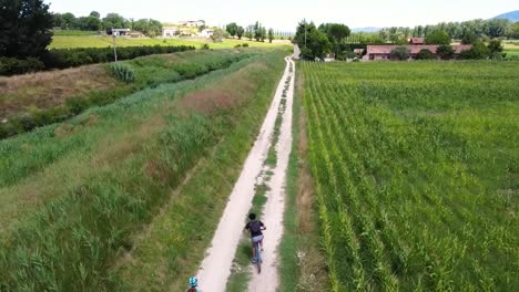 aerial shot chasing a couple of cyclists pedaling on a dirt path near a wide field