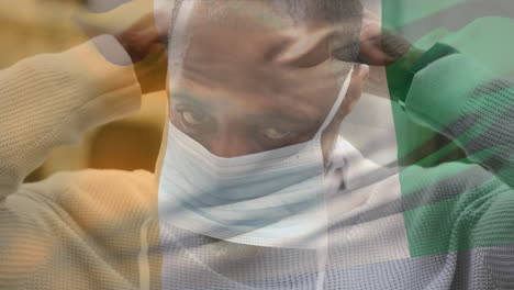 animation of flag of ivory coast waving over man wearing face mask during covid 19 pandemic