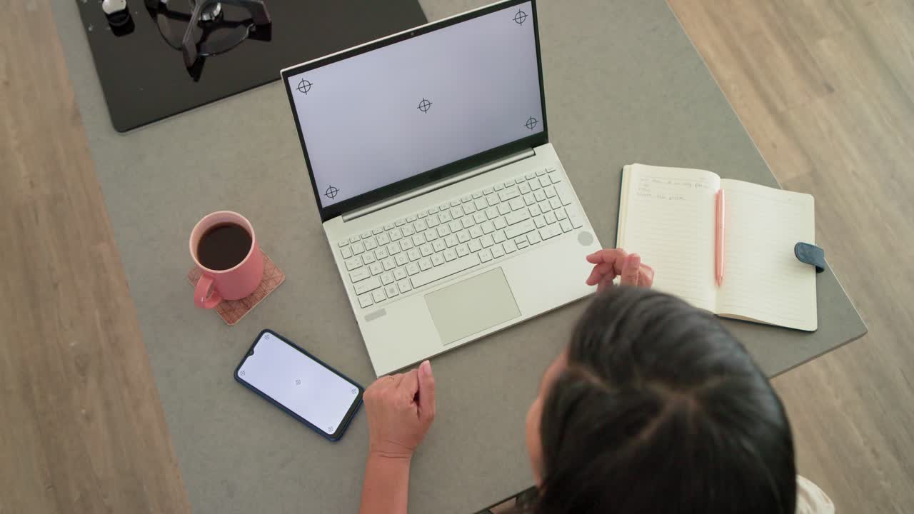 Sitting Asian woman is gesturing toward notes as laptop is showing markers while working near phone