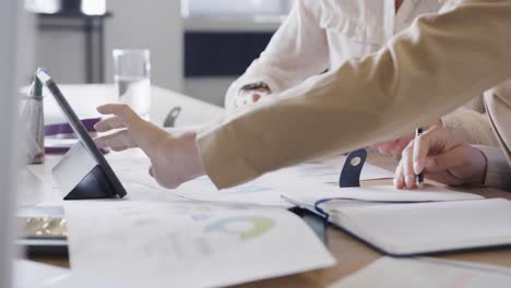 hands of diverse female colleagues in discussion using tablet in office, slow motion