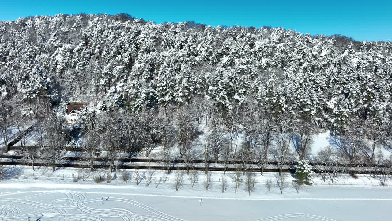 ポーランドのグダニスク、澄み切った青空の下、線路沿いに広がる真っ白な新雪に覆われた鬱蒼とした松林の壮大な空撮。