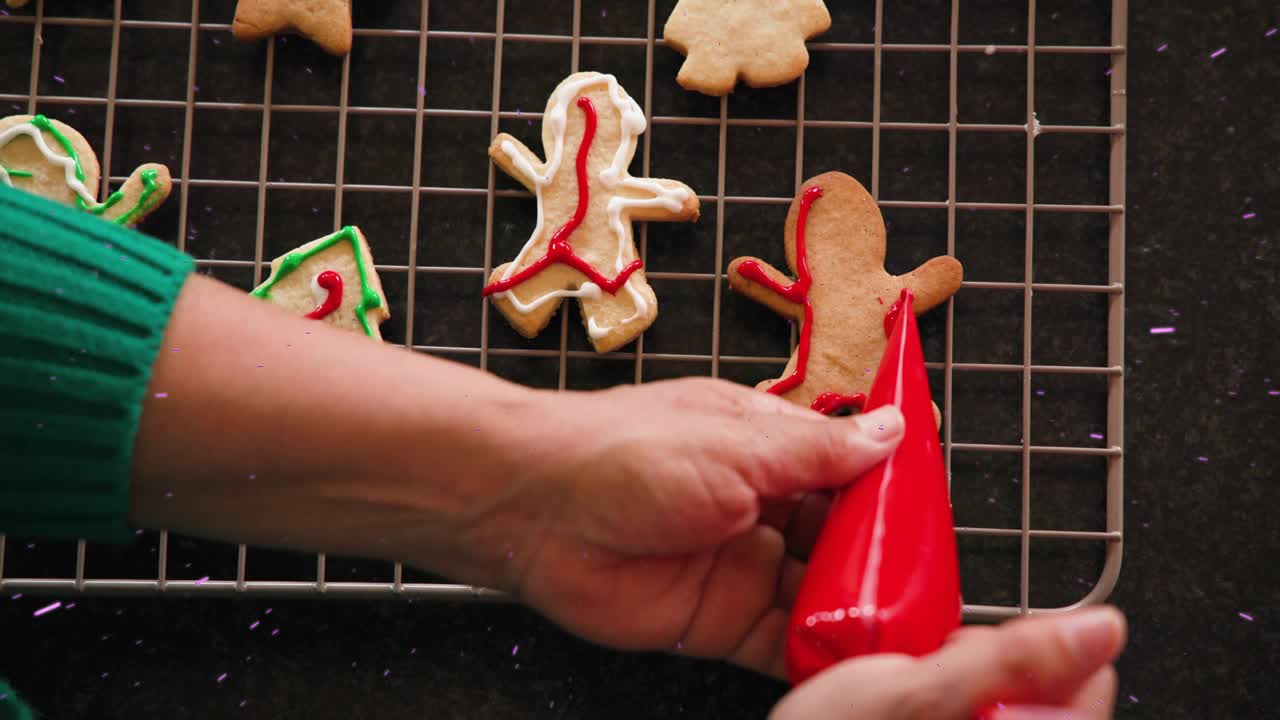 Female baker's hand entering with piping bag, outlining gingerbread man in red for festive baking