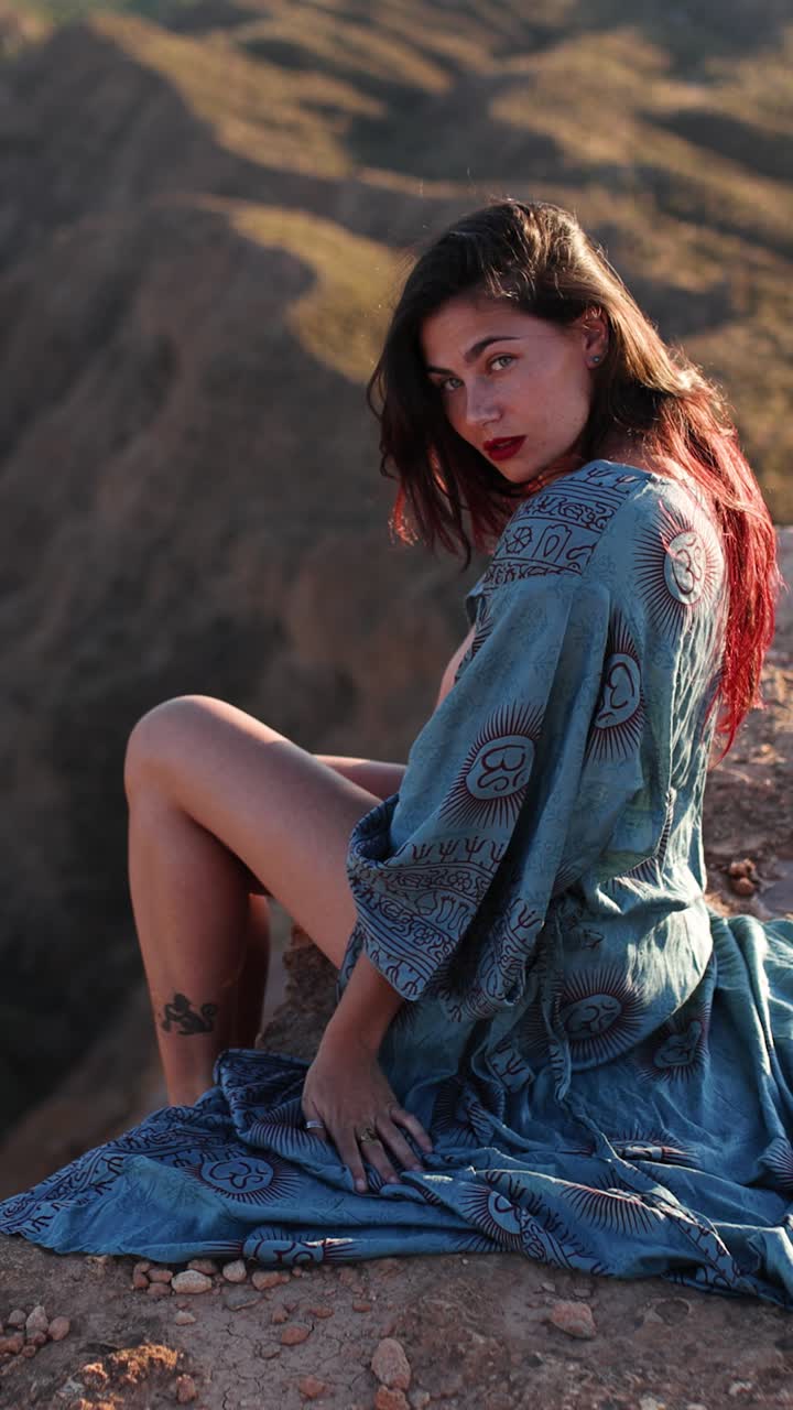 Woman in a patterned blue dress sitting on a cliff