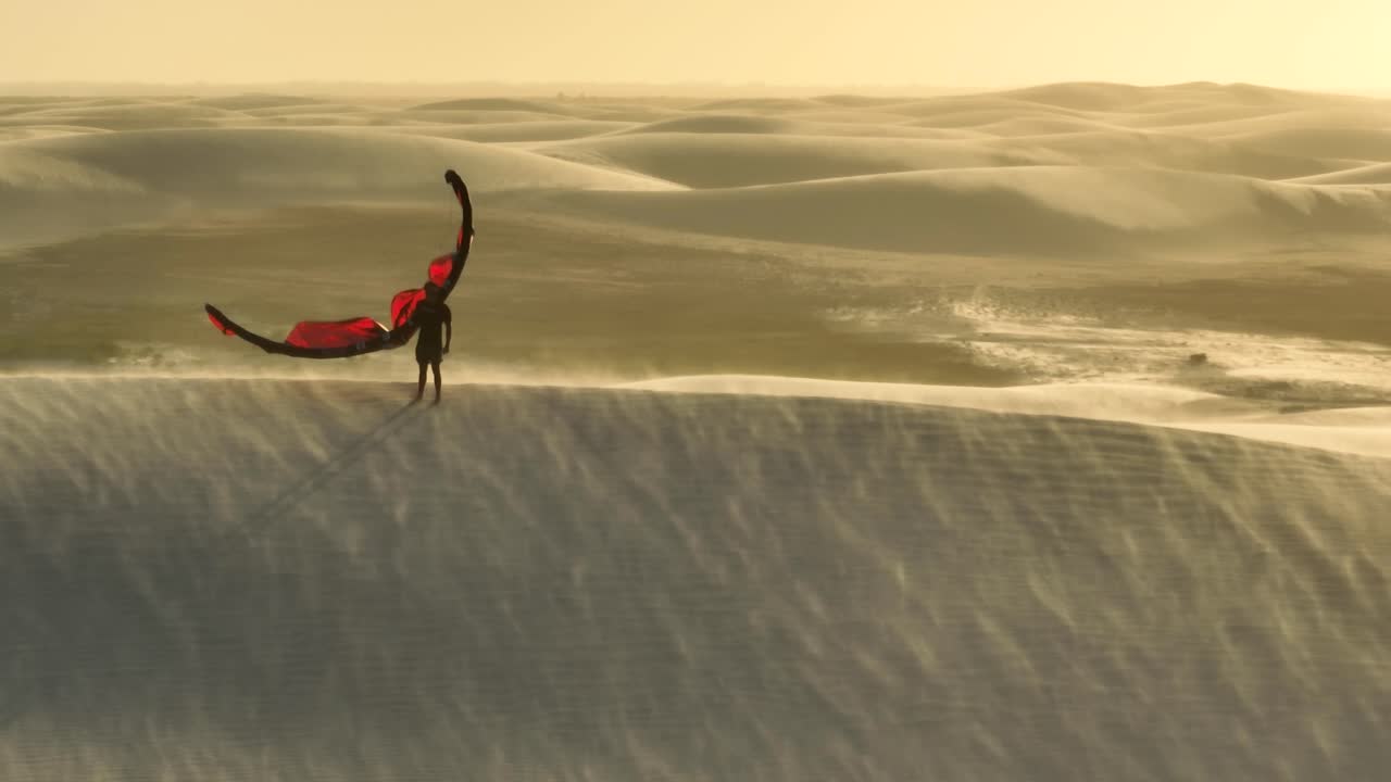 Tracking 360 Degree Aerial Drone Shot of Man Holding Red Kitesurfing Kite During Sunset on a Wind Swept Dune