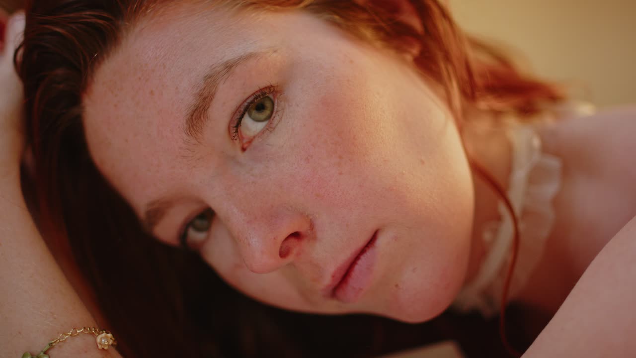Beautiful ginger woman enticingly looking towards camera and playing with her long, red hair