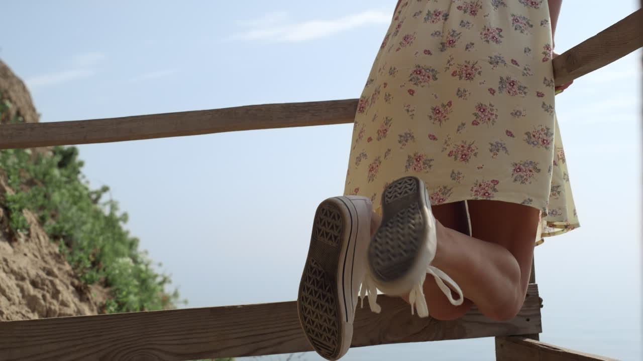Gros plan des jambes minces d'une fille portant des baskets près de l'océan. Une femme appuyée sur l'escalier.
