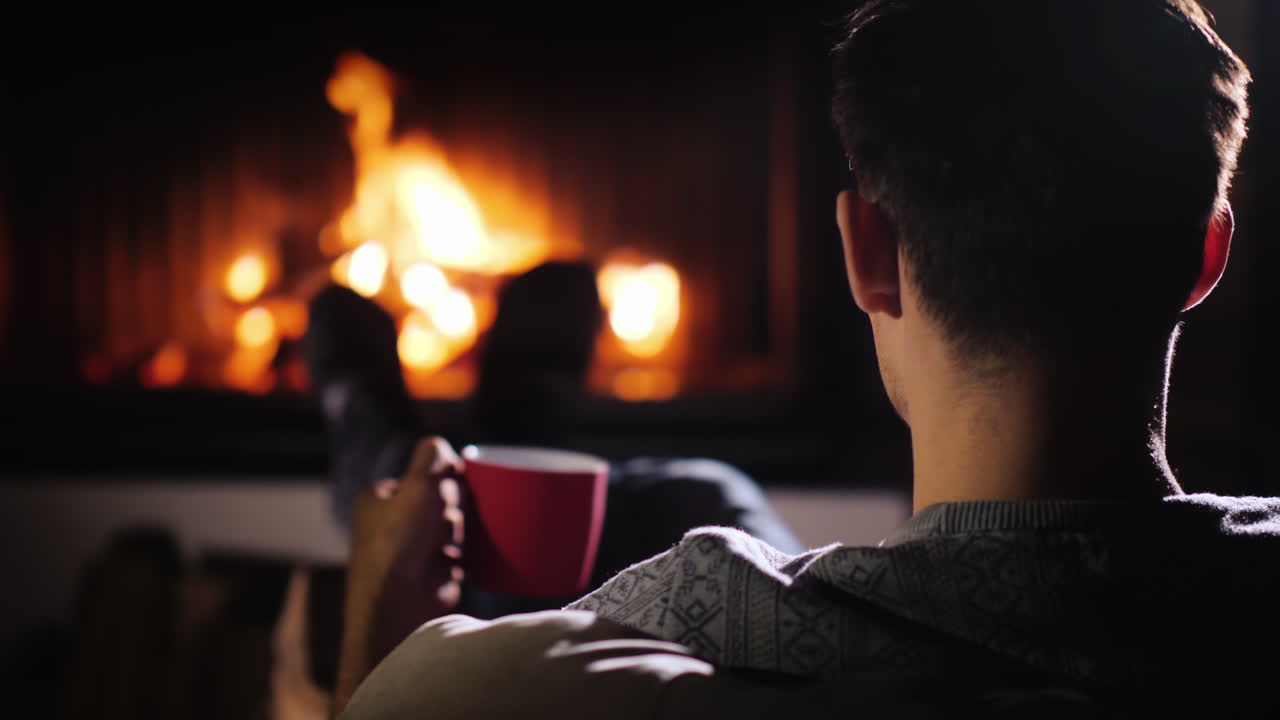 한 청년이 벽난로의 불을 존경하며 차 한 잔을 손에 들고 있다