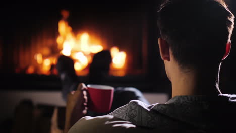 a young man admires the fire in the fireplace holds a cup of tea in his hand