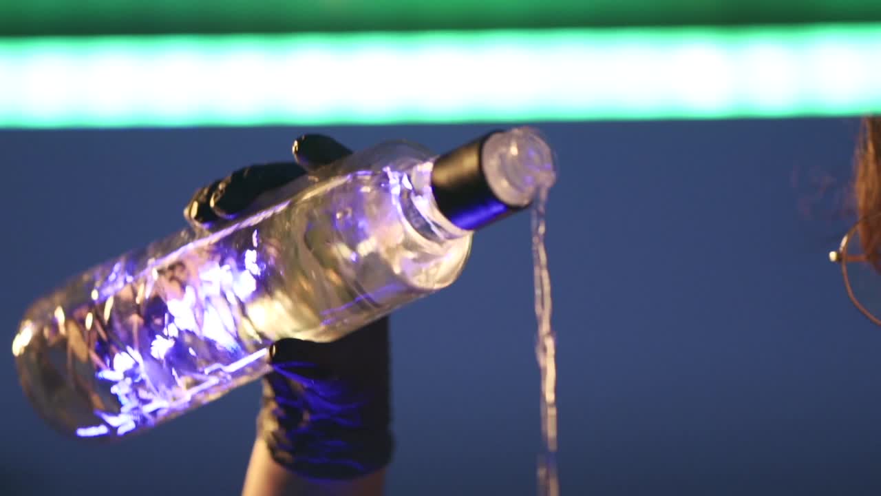 A person pours a bottle of liquor into a glass