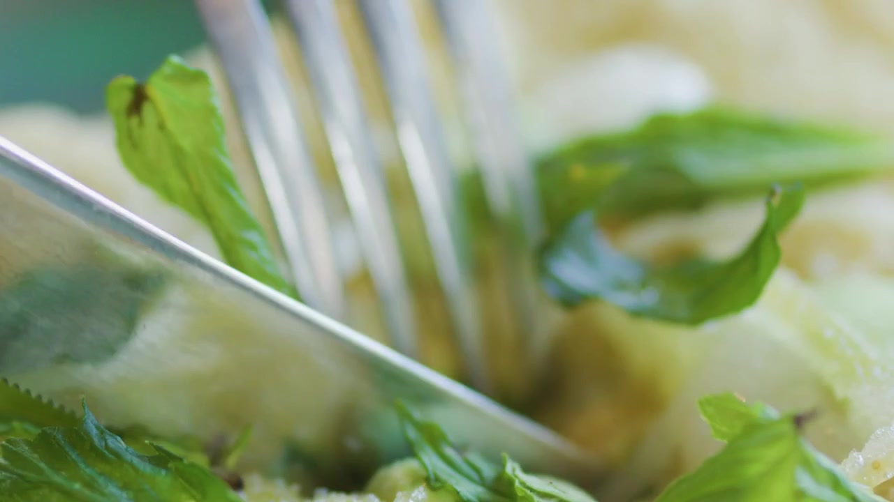Extreme close-up of a silver fork and knife slicing through a garnished seafood appetizer.