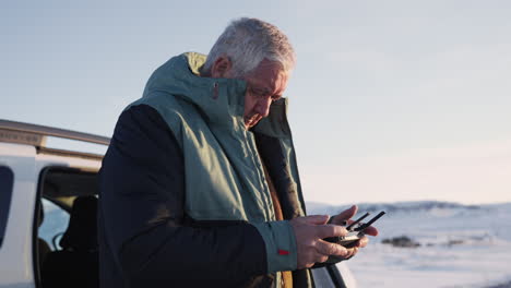 caucasian white hair middle ages male playing with drone controller on snowy landscape