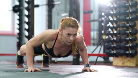 athletic girl trains in the gym with heavy dumbbells. crossfit. a sporty girl performs push-ups from the floor in the gym