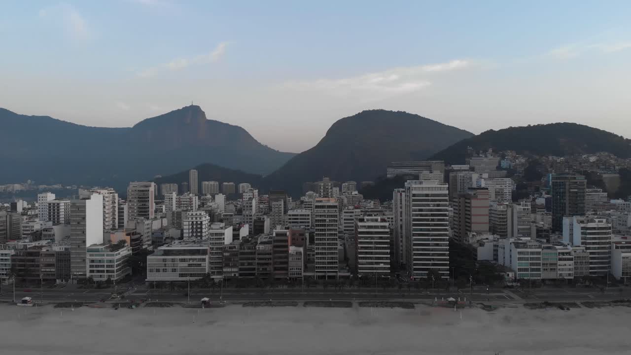 antena retrocediendo desde la playa vacía de ipanema temprano en la mañana revelando las olas del océano en primer plano contra el paisaje urbano más amplio de río de janeiro con la montaña corcovado en el fondo
