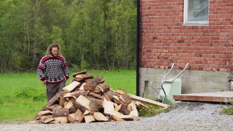 long-haired guy standing in front of heap chopped woods