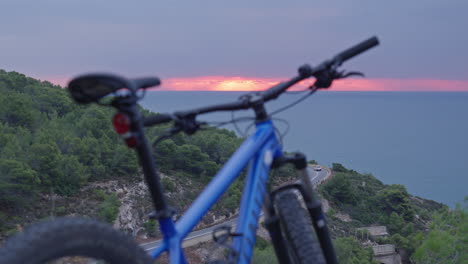Time-lapse-of-mountain-bike-parked-in-wild-as-cars-drive-down-below-and-red-morning-sun-rises-over-the-horizon