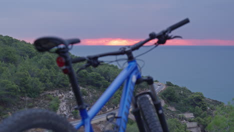 time lapse of mountain bike parked in wild as cars drive down below and red morning sun rises over the horizon