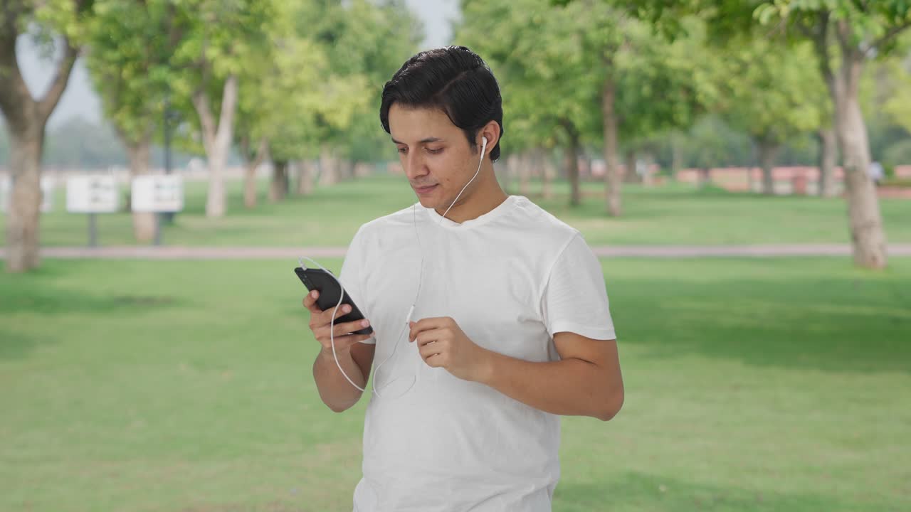 행복한 인디언 남자가 이어폰으로 노래를 듣고 그루브를 하고 있습니다.