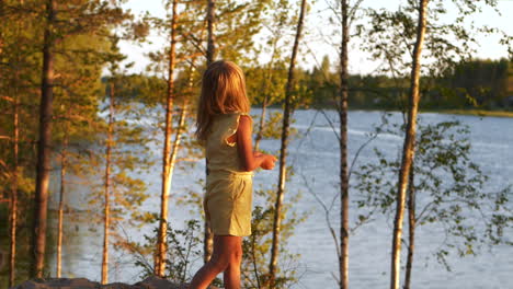 blonde girl standing between trees looking out at lake, behind