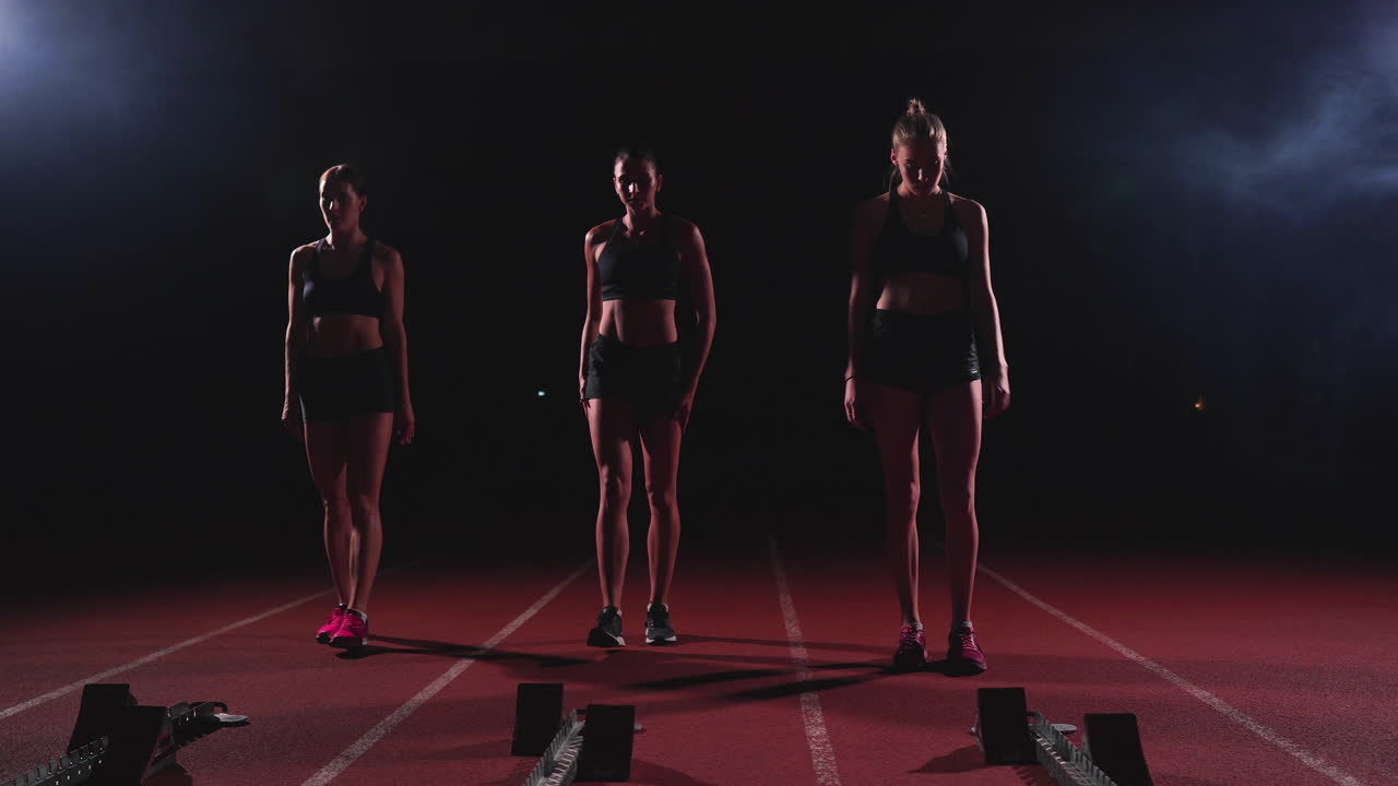 육상 트랙의 여자 달리기 선수들이 경주 전에 출발 블록에 앉아 있습니다. 슬로우 모션으로.