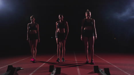 Female-runners-at-athletics-track-crouching-at-the-starting-blocks-before-a-race.-In-slow-motion.