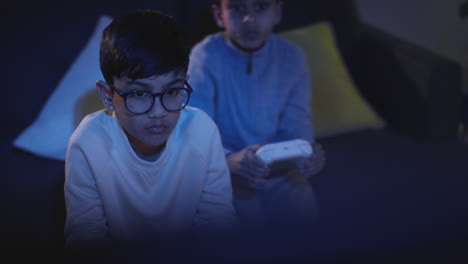 Front-View-Of-Two-Young-Boys-At-Home-Having-Fun-Playing-With-Computer-Games-Console-On-TV-Holding-Controllers-Late-At-Night-2