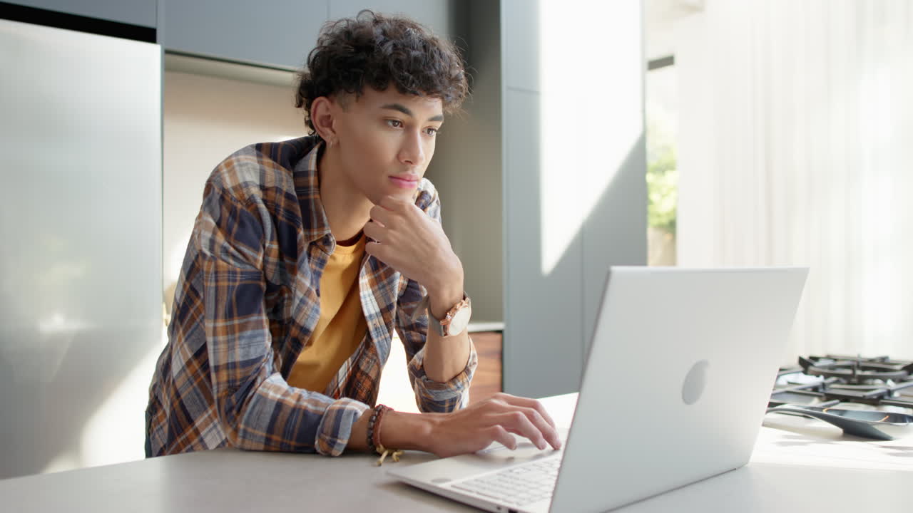 Smiling teenage boy using laptop at home, looking at camera confidently