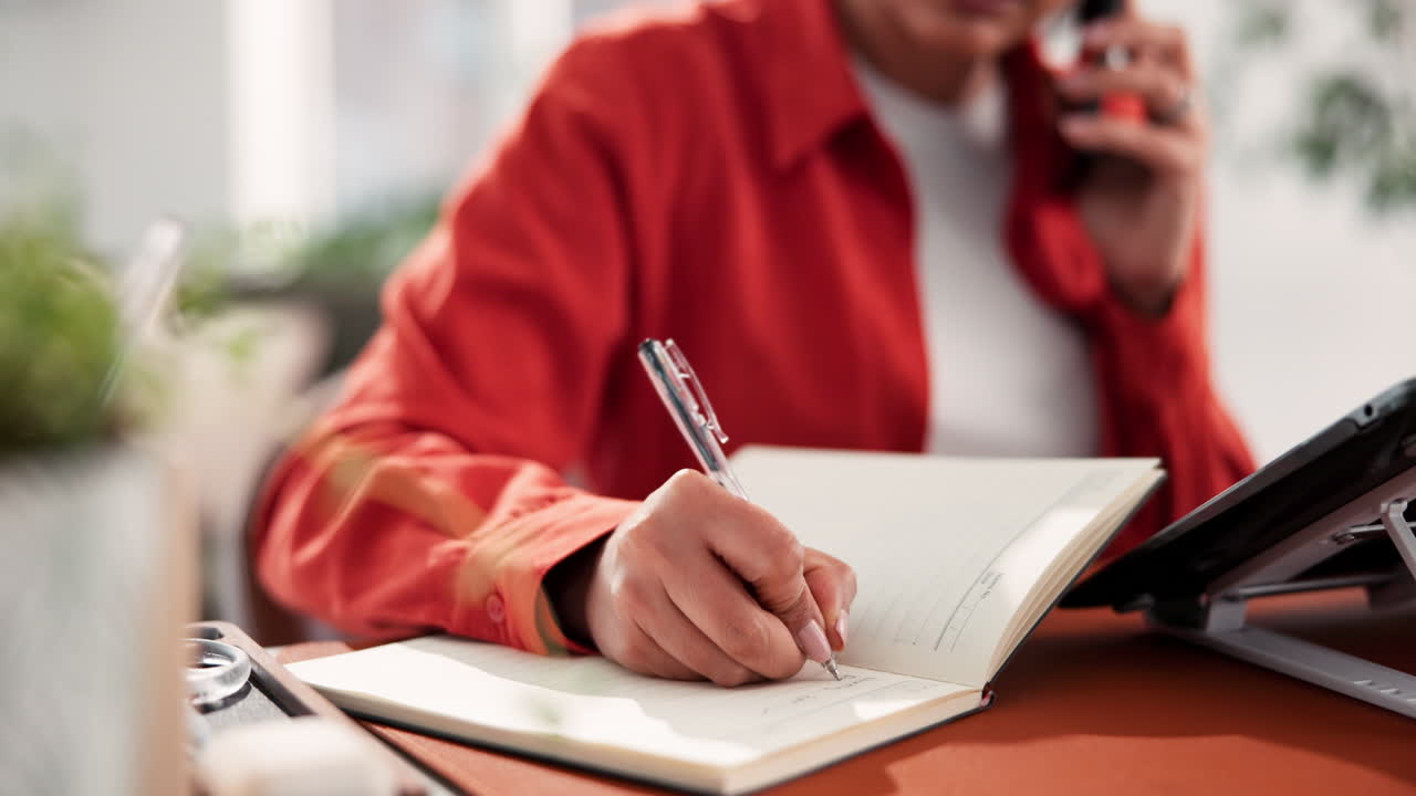 Woman writing in notebook while on phone