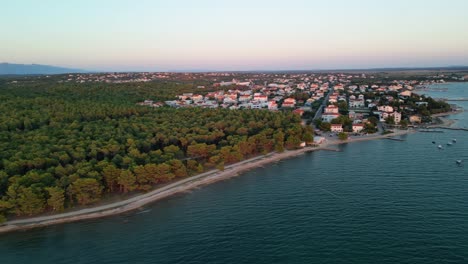 Vista-Aérea-Sobre-El-Prístino-Bosque-De-Pinos-Y-El-Pueblo-De-Vrsi-Mulo,-En-La-Región-De-Zadar,-Croacia,-A-La-Luz-Del-Atardecer-De-Verano.